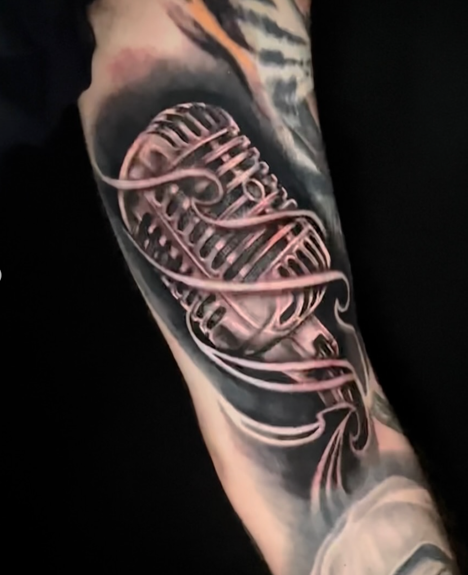 Black-and-grey vintage microphone tattoo with flowing linework